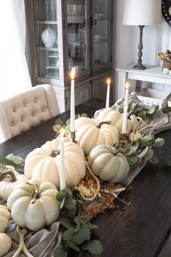 Podzimní dekorace stolu s dýní, bílými svíčkami, bílými dýněmi, perlovým náhrdelníkem, eukalyptovými listy