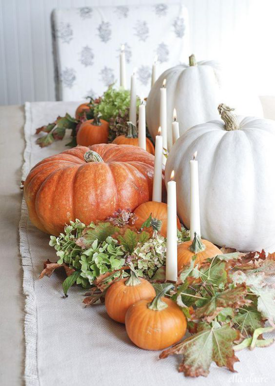 Podzimní dekorace stolu s dýněmi bílé a oranžové dýně různé velikosti svíčky zelené listy