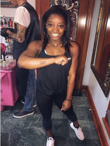 Simone Biles demonstruoja savo šviežią olimpinių žiedų tatuiruotę. Nuotrauka: Simone Biles/„Instagram“. Medalius laimėjusi gimnastė savo „Instagram“ paskyroje taip pat pasidalino savo naujos tatuiruotės nuotrauka, kurioje buvo parodytas žiedų rinkinys, užrašytas rašalu dešinėje dilbio išorėje, netoli riešo.