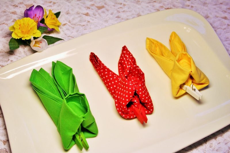 מפיות צבעוניות הוראות קיפול ארנב פסחא בצבעים בהירים שונים כמבטא על השולחן